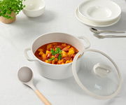 Ein Kochtopf mit Deckel, gefüllt mit einem Eintopf aus Gemüse und Wurst, auf einem Tisch mit weißem Tischtuch. Perspektive von oben.