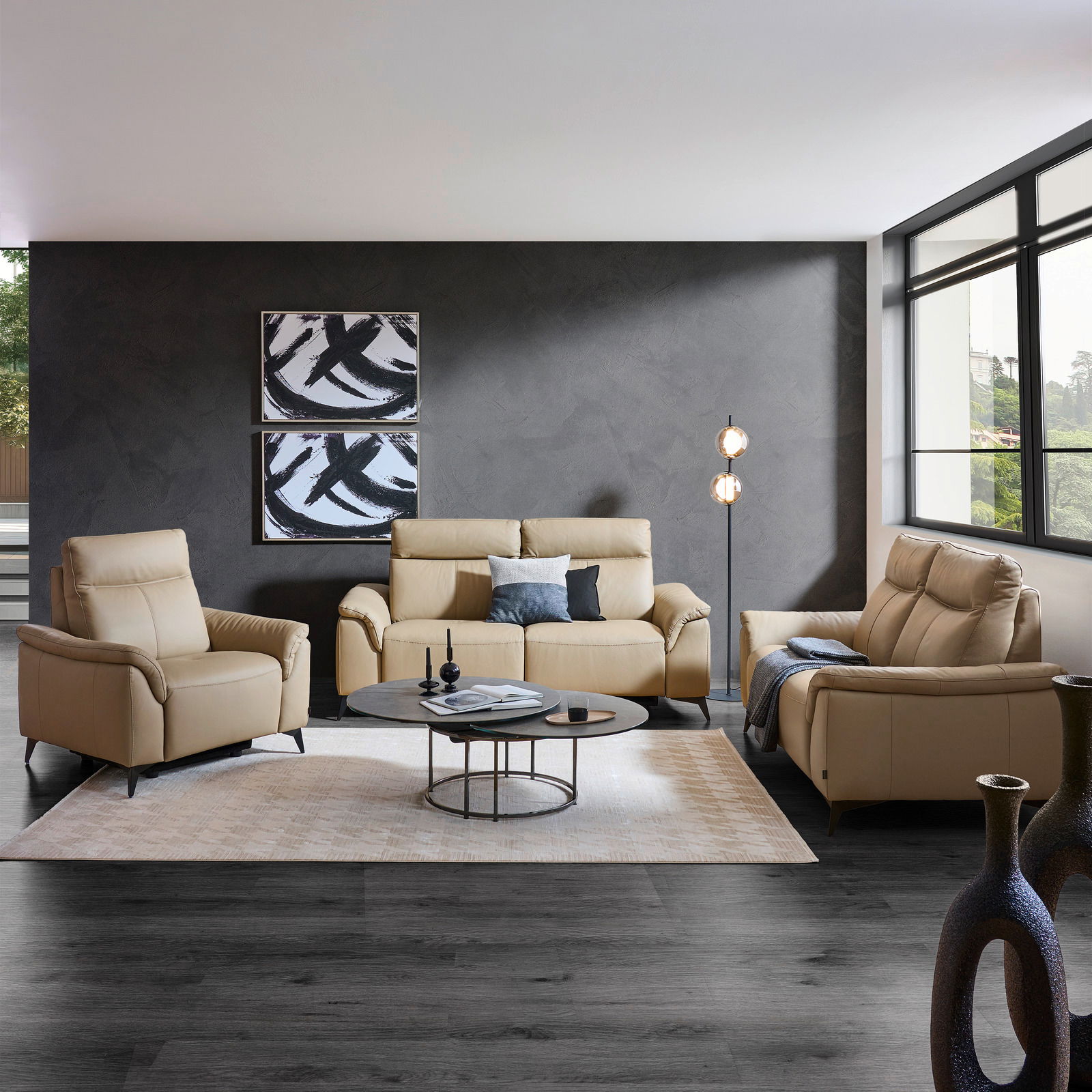 Emilio Belluti Sofa 3er ALAN Wohnzimmeransicht mit beigem Ledersofa-Set bestehend aus einem 3-Sitzer, einem 2-Sitzer und einem Sessel, vor einer grauen Wand mit moderner Kunst, auf einem hellen Teppich mit Couchtisch und Stehlampe.