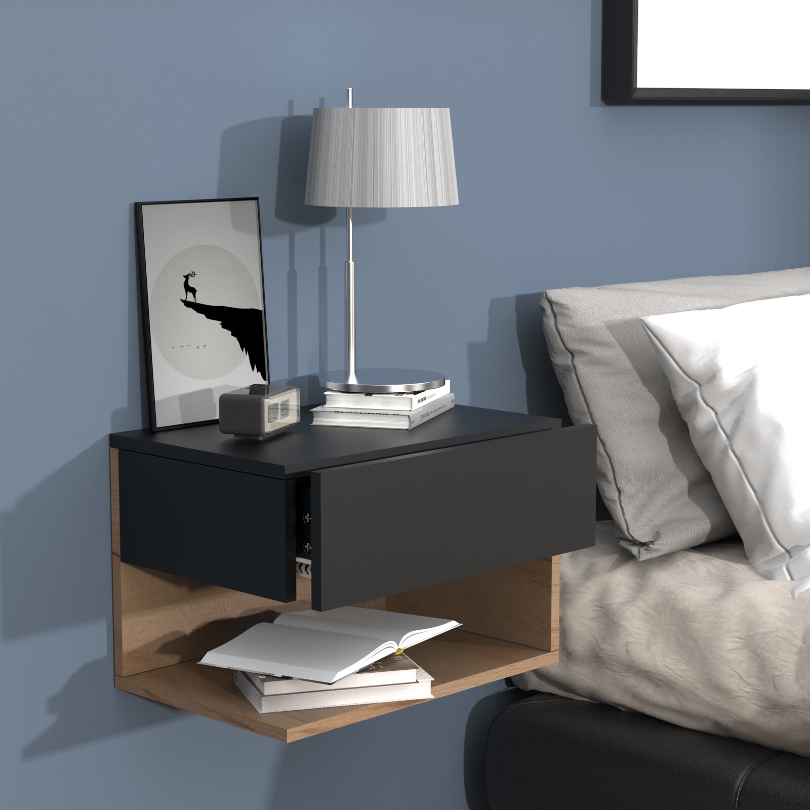 Modernes, schwebendes Nachttisch-Wandregal in Schwarz und Holzoptik mit zwei Schubladen neben einem Bett, darauf Lampe, Bilderrahmen und Bücher, Ansicht schräg von vorn.