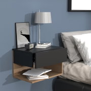 Modernes, schwebendes Nachttisch-Wandregal in Schwarz und Holzoptik mit zwei Schubladen neben einem Bett, darauf Lampe, Bilderrahmen und Bücher, Ansicht schräg von vorn.