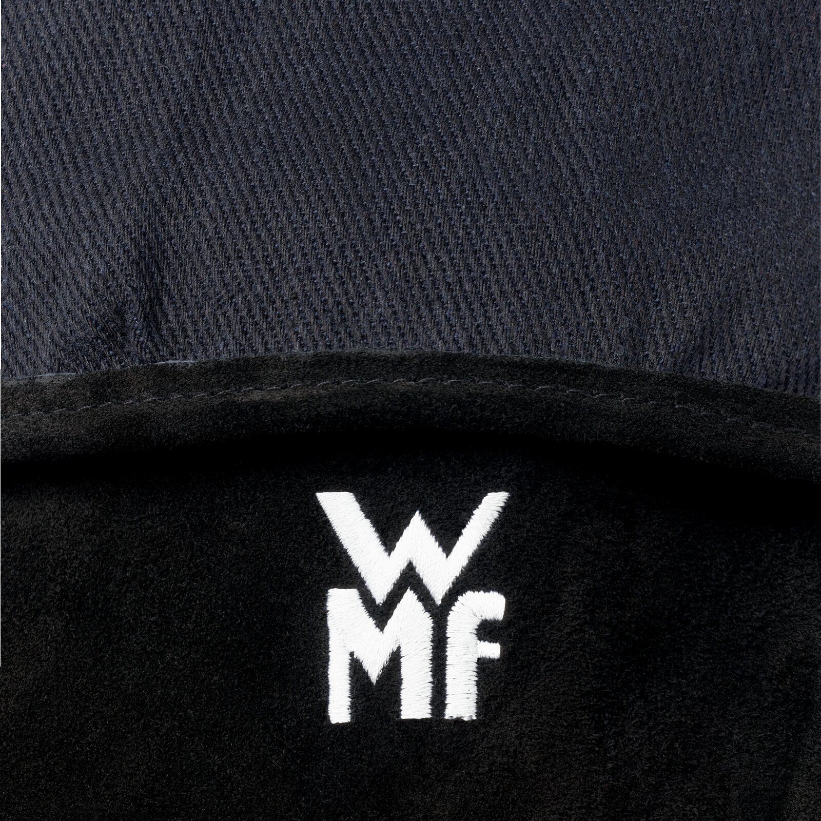 Detailfoto van bovenaf van een zwarte, zachte stof met een wit geborduurd WMF-logo op een donkere achtergrond