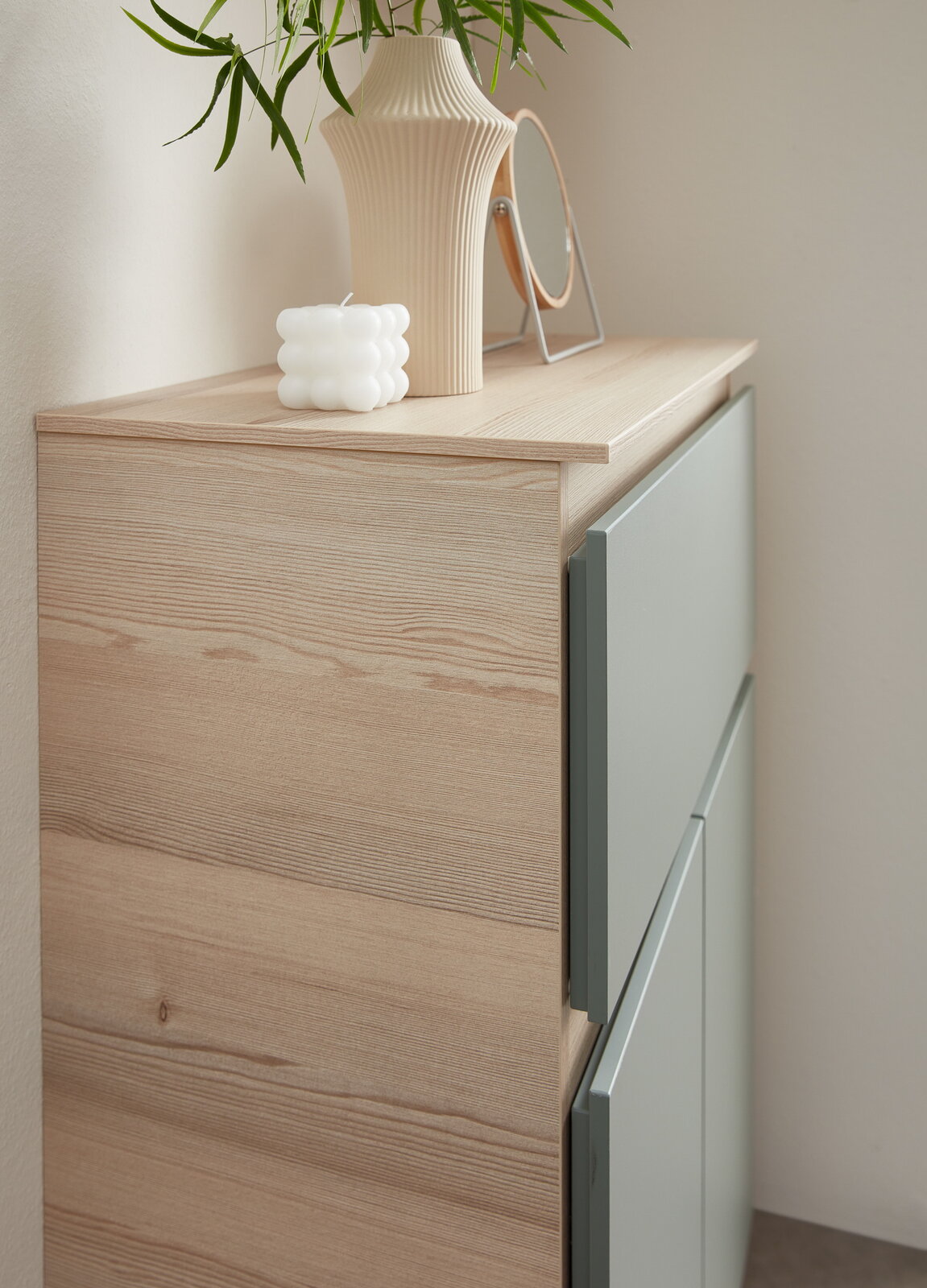 Nahaufnahme eines Unterschranks mit Abdeckplatte aus Holz, dekoriert mit einer Vase, einem Spiegel und einer Kerze, seitliche Perspektive.