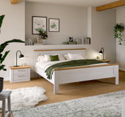 Modernes Doppelbett aus weißem Holz mit naturfarbenen Akzenten an Kopf- und Fußteil, grüne Tagesdecke und Nachttische im Schlafzimmer; Perspektive: frontale Ansicht leicht von links.