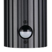 Close-up van een zwarte buitenwandlamp met geribbeld oppervlak en ingebouwde bewegingssensor.