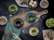 Draufsicht (Flatlay) auf rustikale Kaffeetafel mit mehreren farbigen Espresso- und Kaffeetassen auf Holzbrett, Löffeln, Gebäck, Gläsern und Deko auf dunklem Tisch