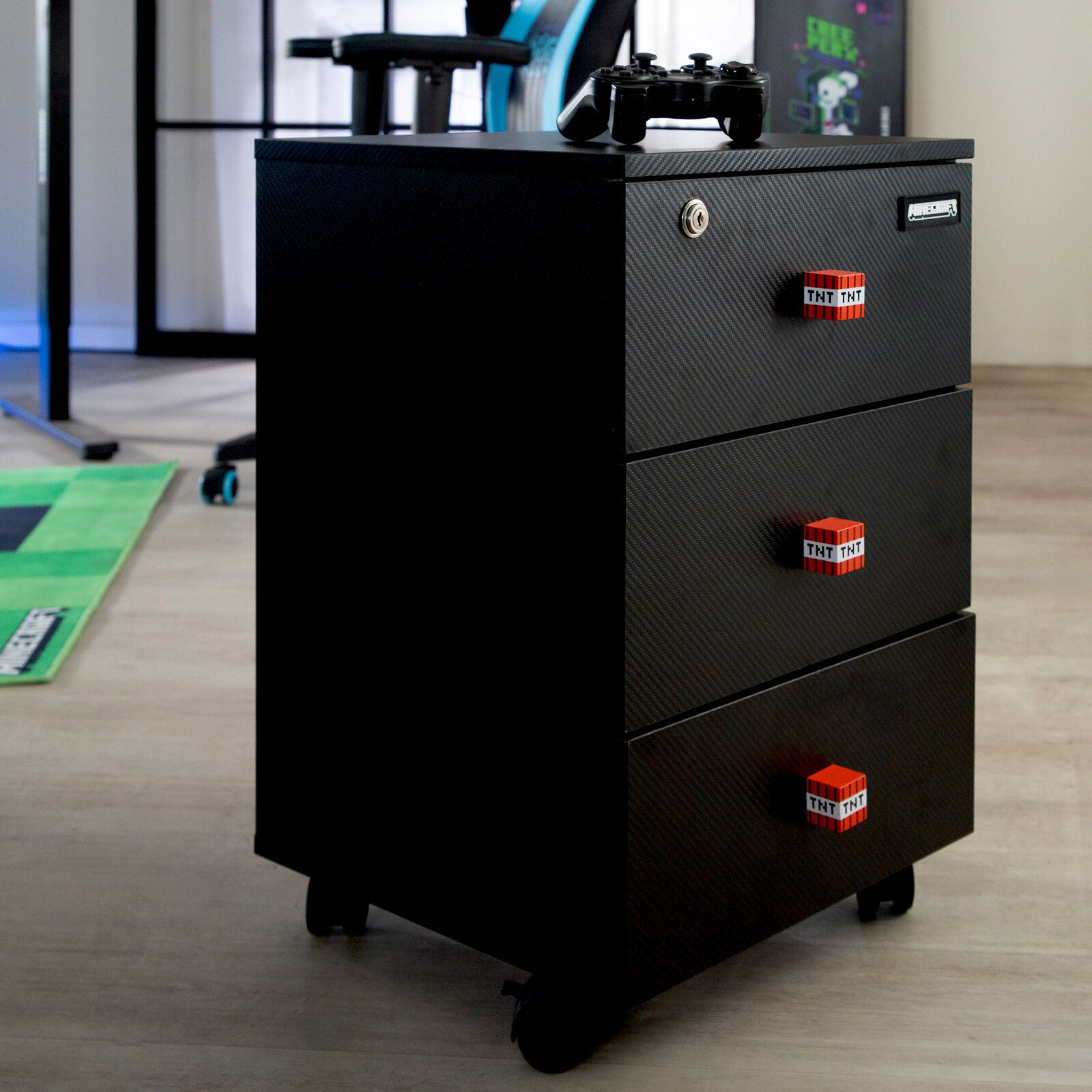 Schwarzer Rollcontainer mit drei Schubladen in Carbon-Optik und roten TNT-Griffen, mit Schloss an der oberen Schublade; Perspektive: frontale Dreiviertelansicht von links auf Bodenhöhe.