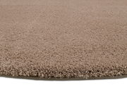 Nahaufnahme eines runden, beigen Teppichs mit weicher, flauschiger Textur, seitliche Perspektive