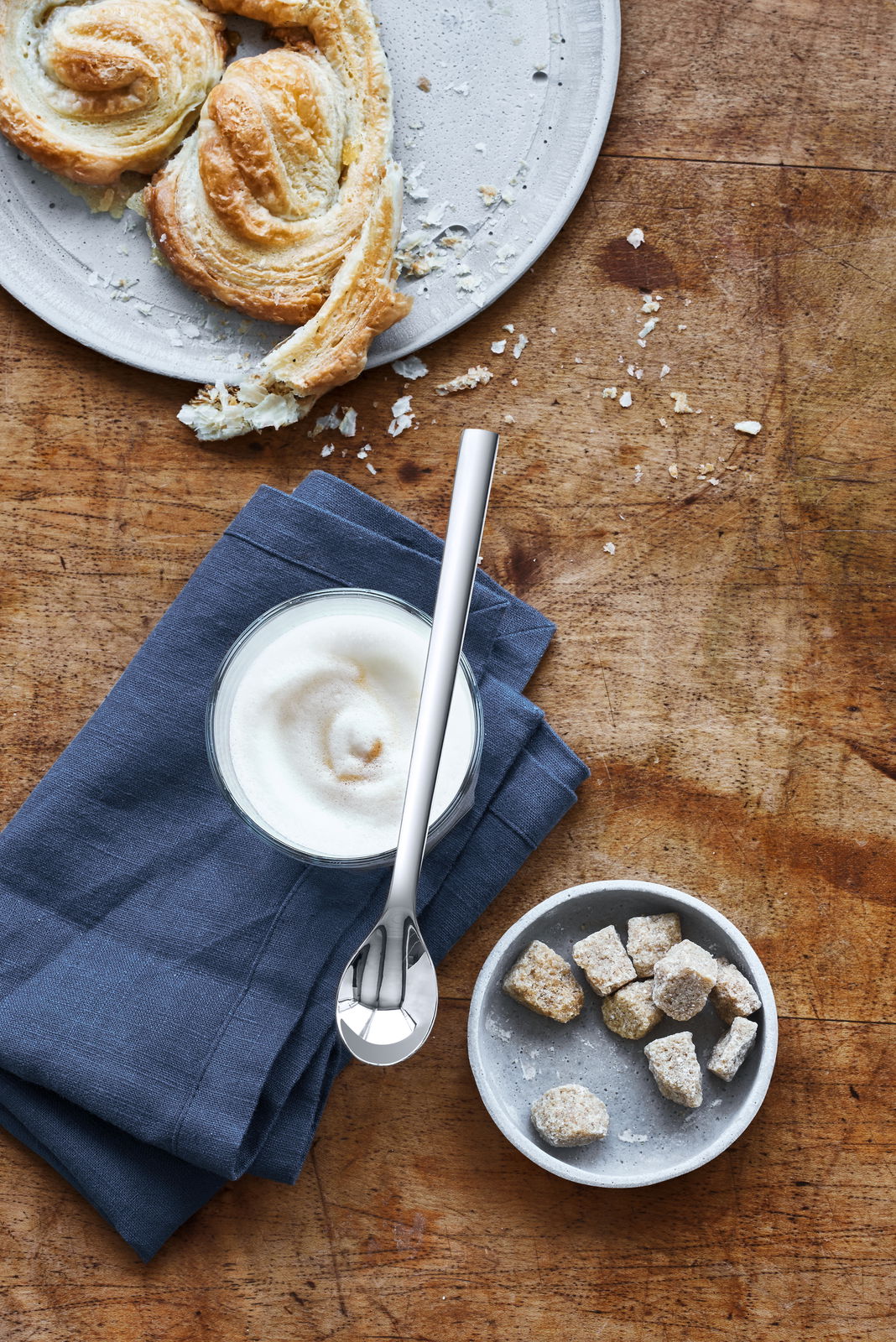 WMF Latte Macchiato-Löffel 6-tlg. NUOVA Latte Macchiato-Löffel Nuova auf einem Holztisch, neben einem Glas mit Milchschaum und Gebäck, aus der Vogelperspektive.