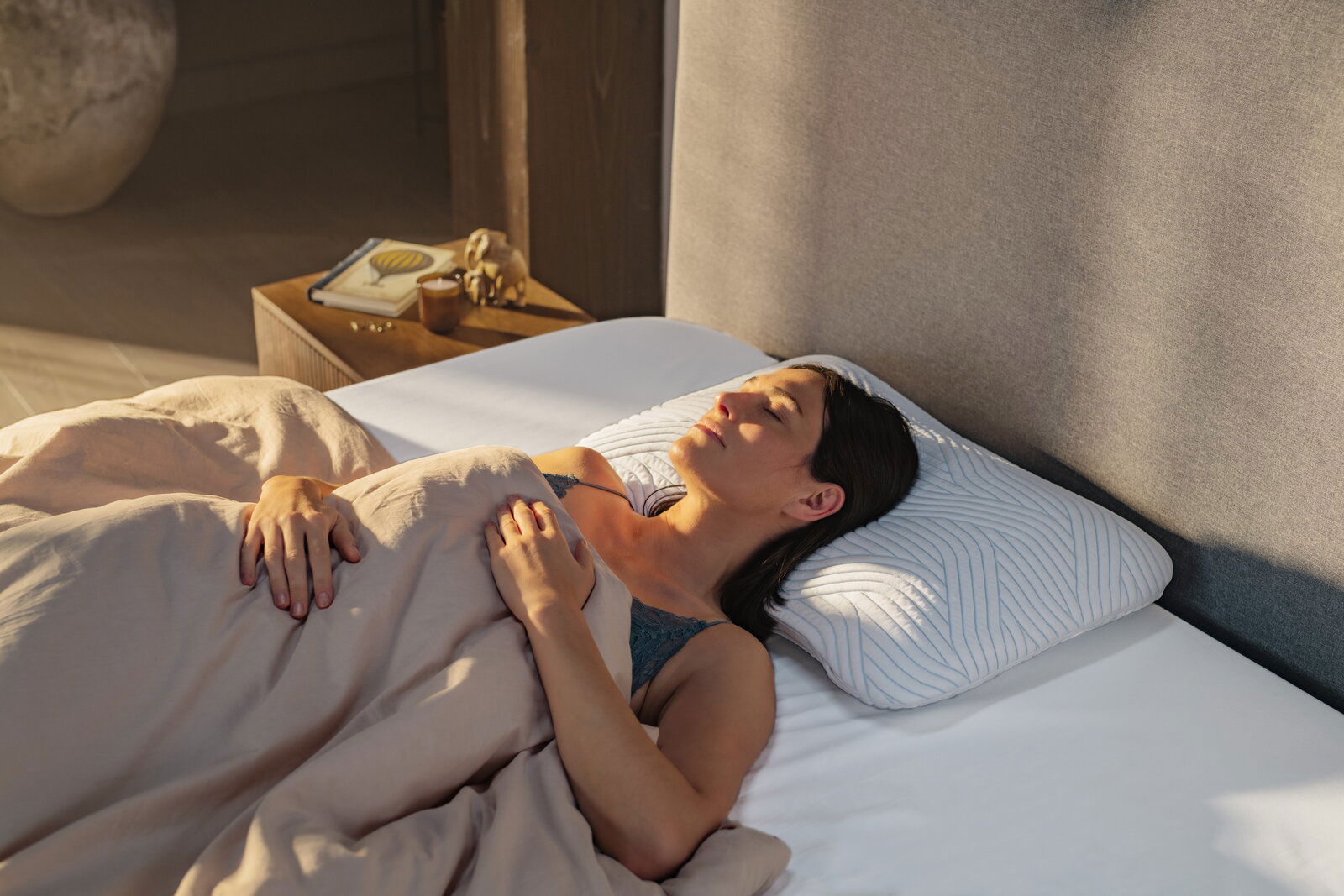 Tempur Schlafkissen ARCH Frau liegt entspannt auf einem Tempur Schlafkissen 63 x 43 cm in einem Bett, seitliche Perspektive