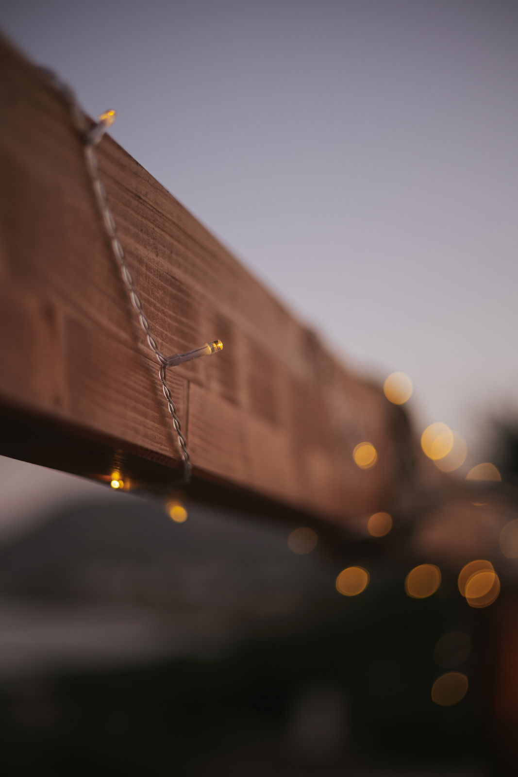 Nahaufnahme einer Outdoor-Solarlichterkette, die um einen Holzbalken gewickelt ist, mit unscharfem Hintergrund in der Abenddämmerung.