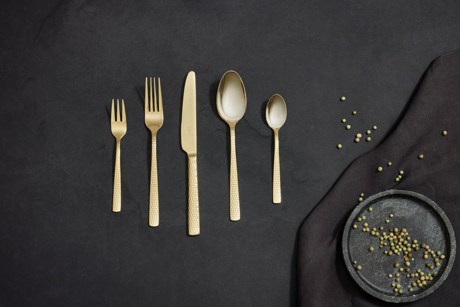 Goldenes Besteckset Sunset 30-tlg. aus der Vogelperspektive auf dunklem Hintergrund mit Pfefferkörnern.