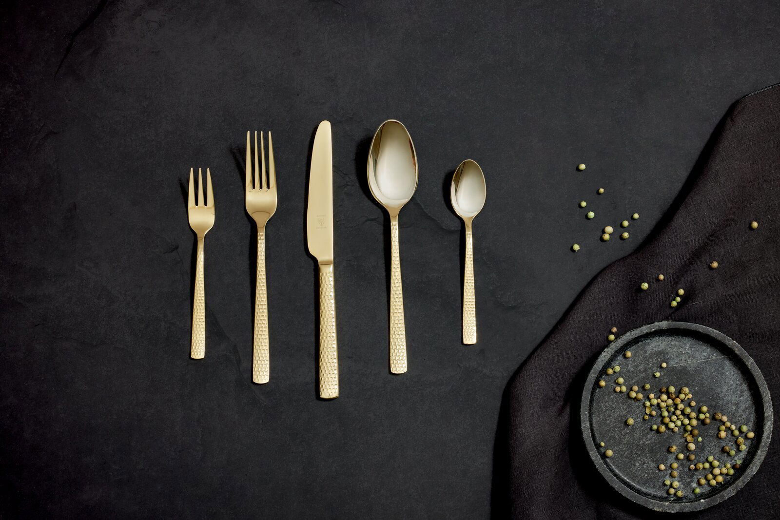 Justinus Besteck 30-tlg. SUNSET Goldenes Besteckset Sunset 30-tlg. aus der Vogelperspektive auf dunklem Hintergrund mit Pfefferkörnern.