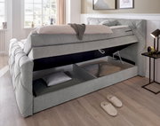 Boxspringbett mit geöffnetem Stauraum, seitliche Perspektive, grauer Stoffbezug, Tageslicht durch Fenster