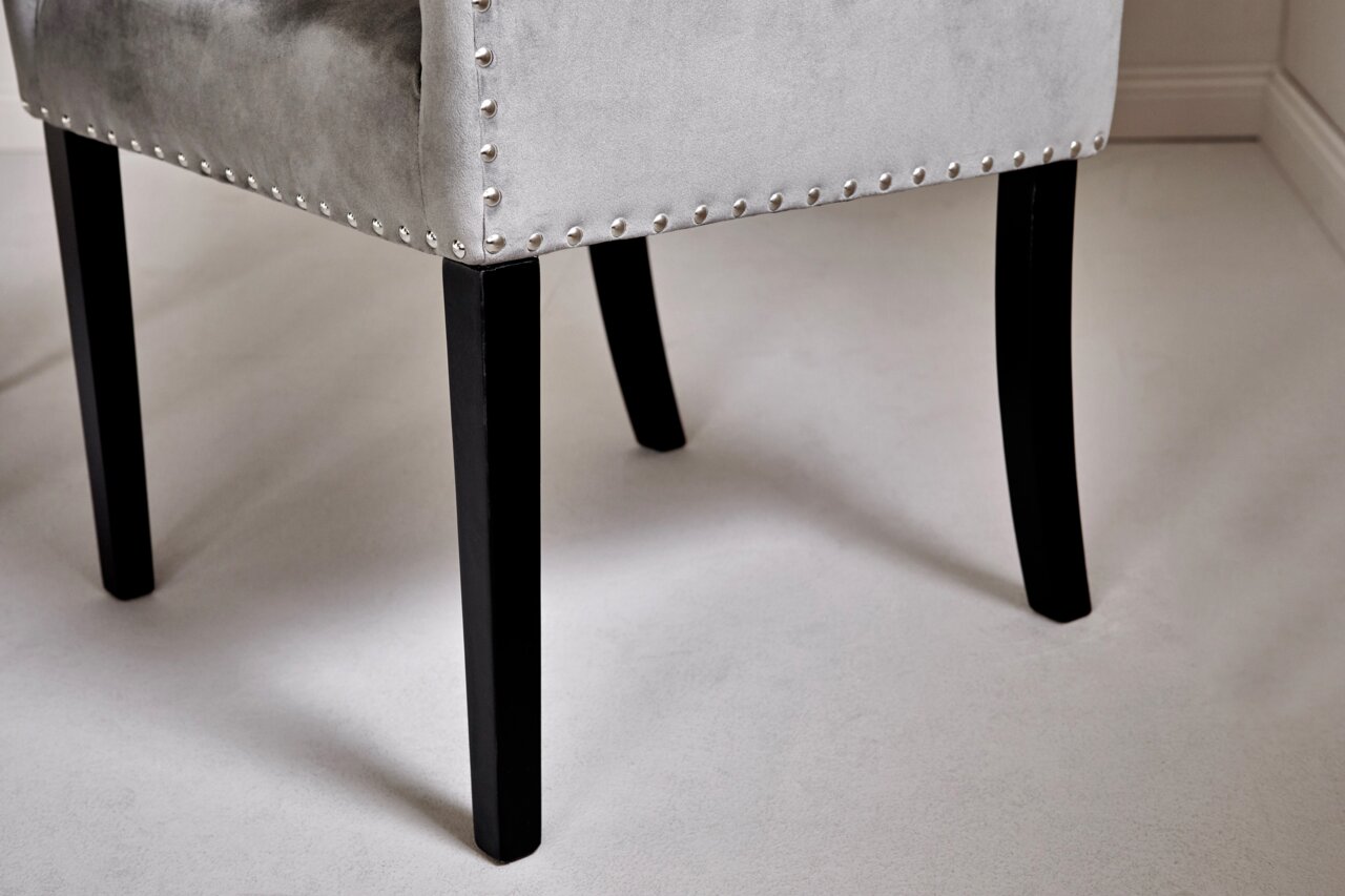 Close-up van een grijze stoel met zwarte poten en zilveren studs, gezien vanaf de zijkant