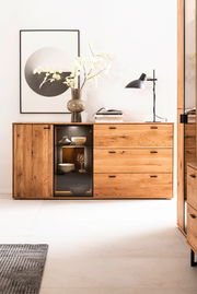 Holz-Sideboard mit Schubladen und Glastür, dekoriert mit einer Vase und Lampe, aus frontaler Perspektive.