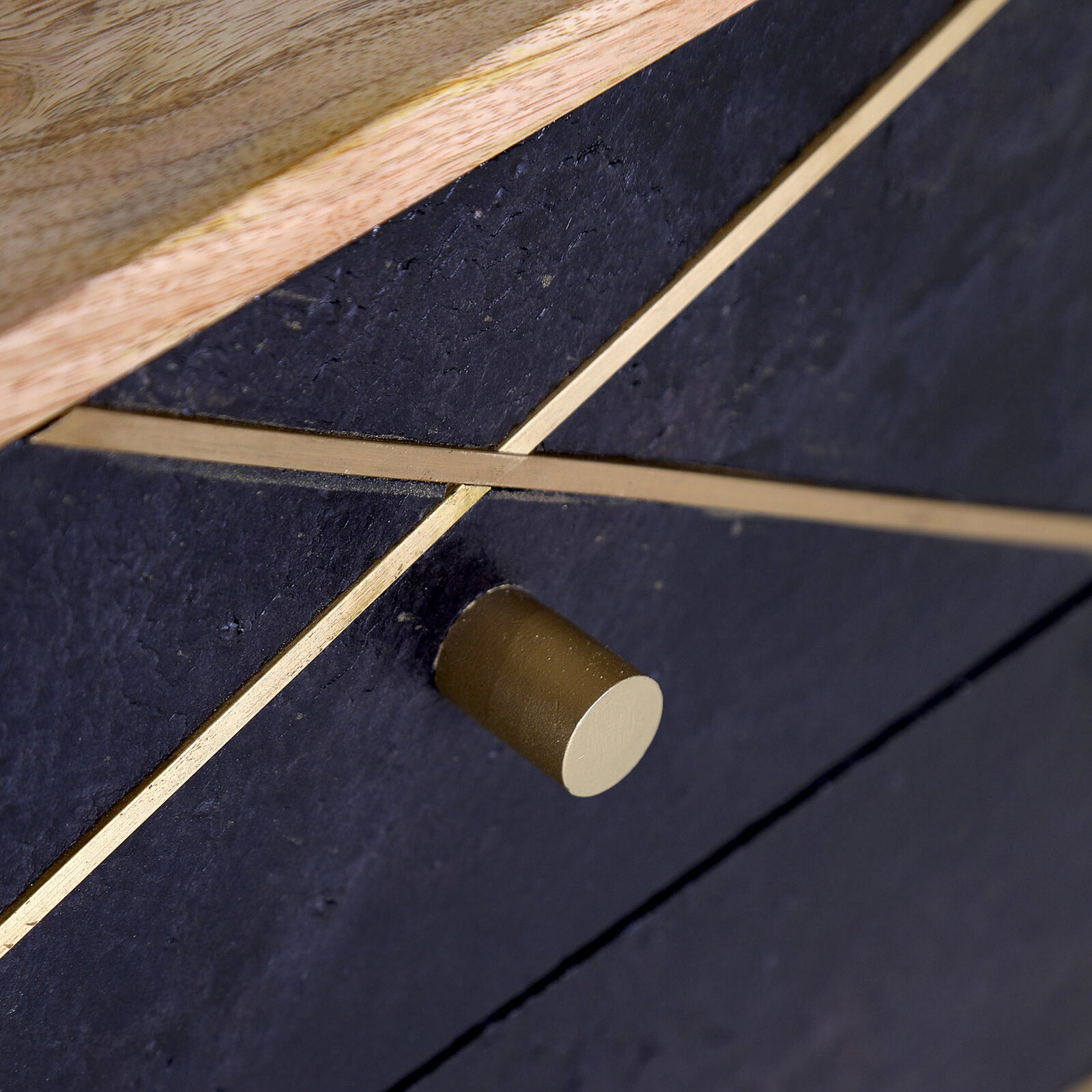 Nahaufnahme einer Nachtkommode mit dunkler Oberfläche, goldenen Zierleisten und einem runden, goldenen Griff, von schräg oben betrachtet.