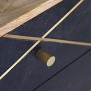 Nahaufnahme einer Nachtkommode mit dunkler Oberfläche, goldenen Zierleisten und einem runden, goldenen Griff, von schräg oben betrachtet.