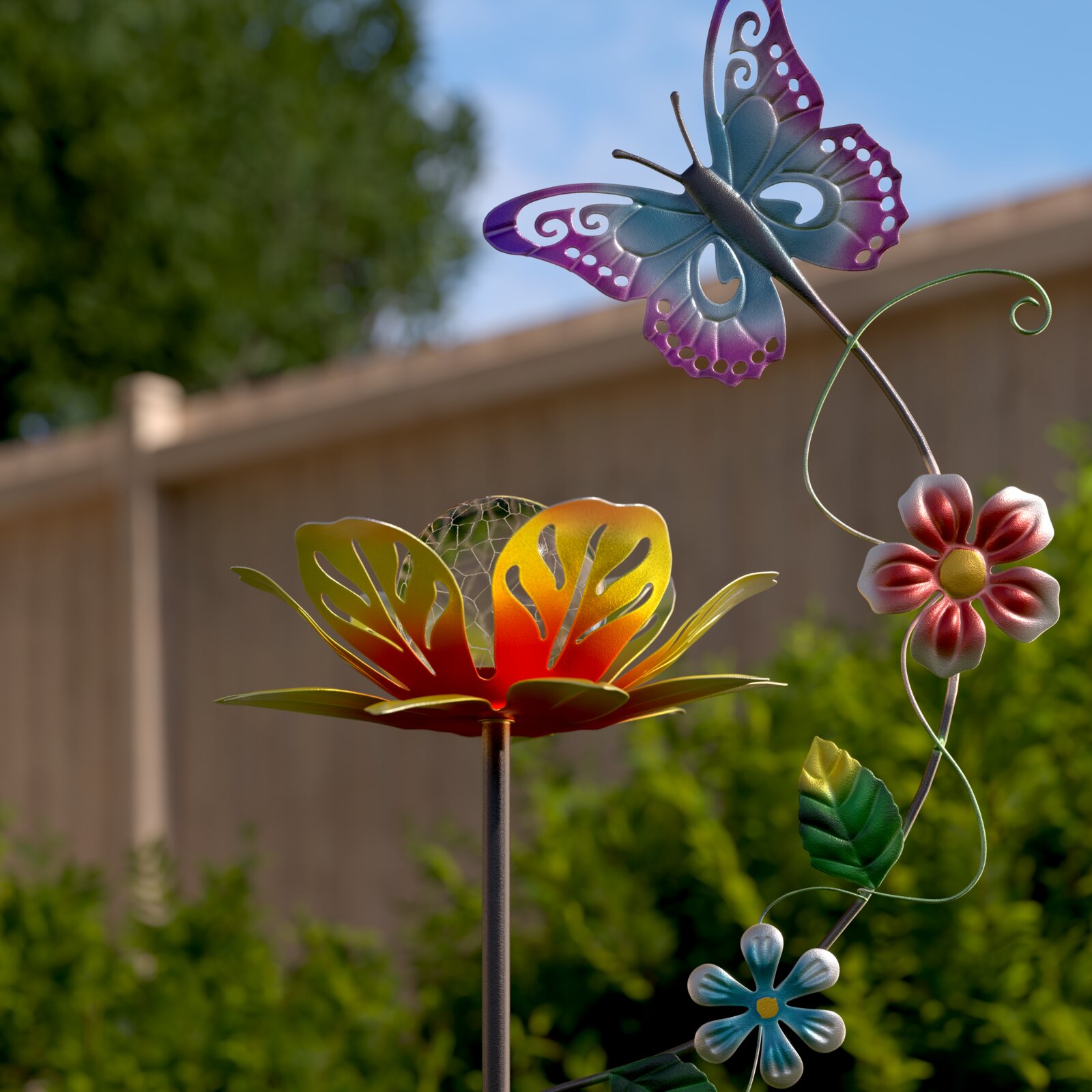 Detailaufnahme aus leicht seitlicher Perspektive: bunter Metall-Gartenstecker mit Schmetterling in Blau-Lila sowie Blumen- und Blattmotiven vor unscharfem Gartenhintergrund