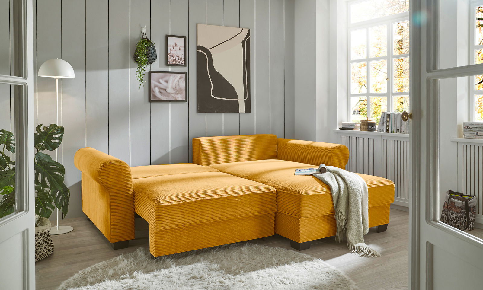 Gemütliche gelbe Rundecke in einem hellen Wohnzimmer, von vorne betrachtet, mit dekorativen Kissen und Decke.