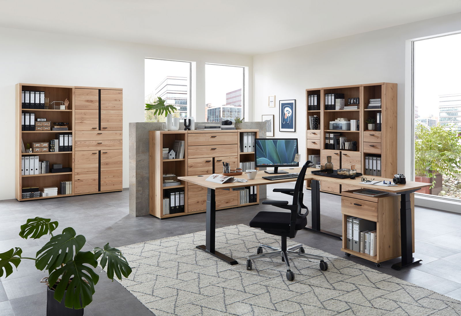 Moderne Büromöbel in einem hellen Raum mit großen Fenstern, bestehend aus Schreibtischen, Aktenschränken und Regalen aus Holz. Perspektive: Frontalansicht.