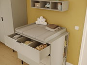 Een commode in een babykamer, met een geopende lade en planken, gefotografeerd vanuit een zijaanzicht.