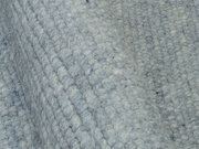 Nahaufnahme eines handgewebten Teppichs in graublauer Farbe mit strukturierter Oberfläche, seitliche Perspektive.