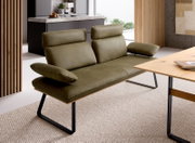 Modernes 2-Sitzer-Sofa in Olivgrün mit verstellbaren Kopfstützen und Armlehnen auf schwarzem Metallgestell, schräg von vorne links in einem hellen Wohnraum fotografiert.