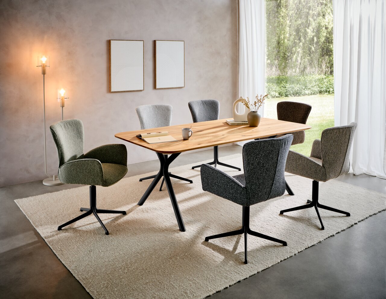 Moderner Esstisch mit Holzplatte und schwarzen Metallbeinen, umgeben von sechs gepolsterten Stühlen in verschiedenen Grautönen, in einem hellen Raum mit großen Fenstern und stilvoller Dekoration. Perspektive: seitliche Ansicht.