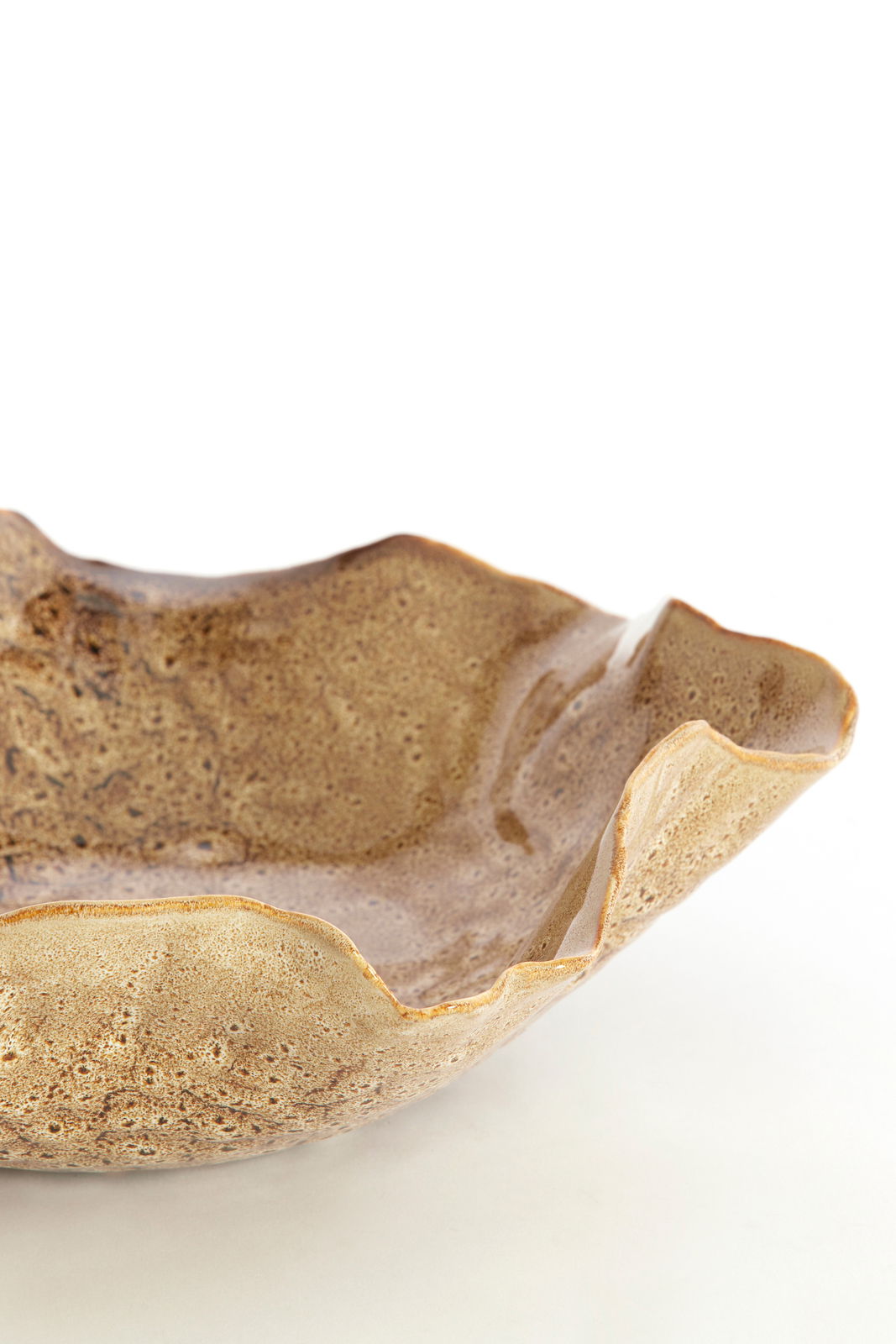 Nahaufnahme einer dekorativen, wellenförmigen Schale aus Keramik in erdigen Brauntönen, seitliche Perspektive.