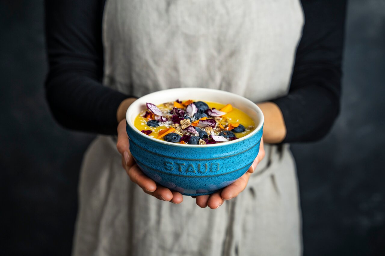 Person hält eine türkisfarbene Schüssel mit frischem Obst und Müsli, Vorderansicht