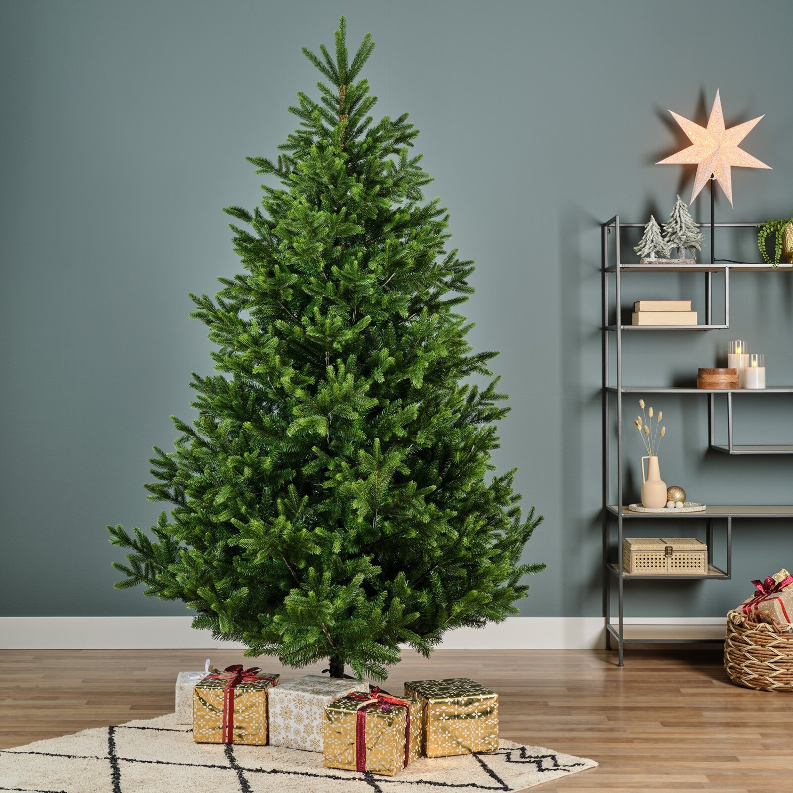 Vooraanzicht van een volle, groene kerstboom in een modern interieur, met feestelijk ingepakte cadeaus eronder en een verlichte ster op de achtergrond.