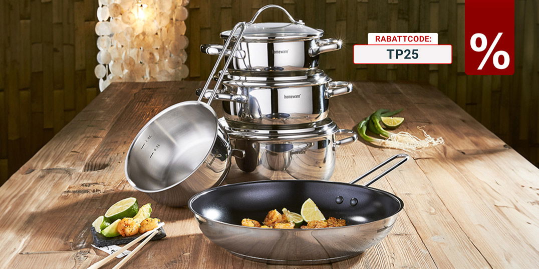 Edelstahl-Topfset und Pfanne auf Holztisch, dekoriert mit Speisen, Limetten und Gemüse in warm beleuchteter Küche