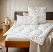 Een gezellige slaapkamer met een bed dat is opgemaakt met een wit vier seizoenen-dekbed en bijpassende kussens, in close-up.