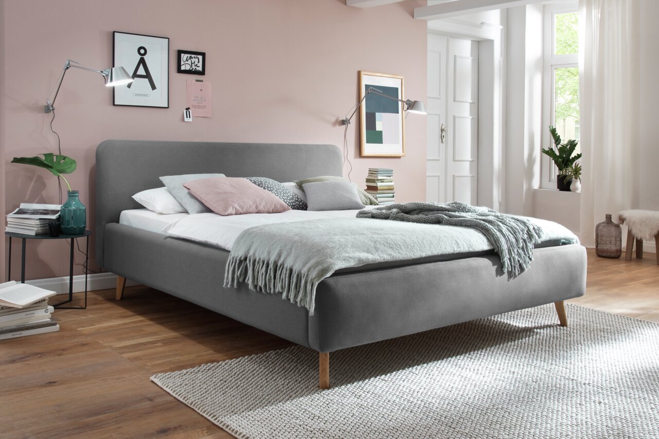 Graues Polsterbett in einem modernen Schlafzimmer, seitliche Perspektive, mit dekorativen Kissen und Decken.