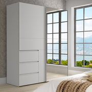 Moderner weißer Schwebetürenschrank mit zwei Türen, einer davon mit Spiegel, in einem hellen Raum mit Blick auf große Fenster. Perspektive von schräg vorne.