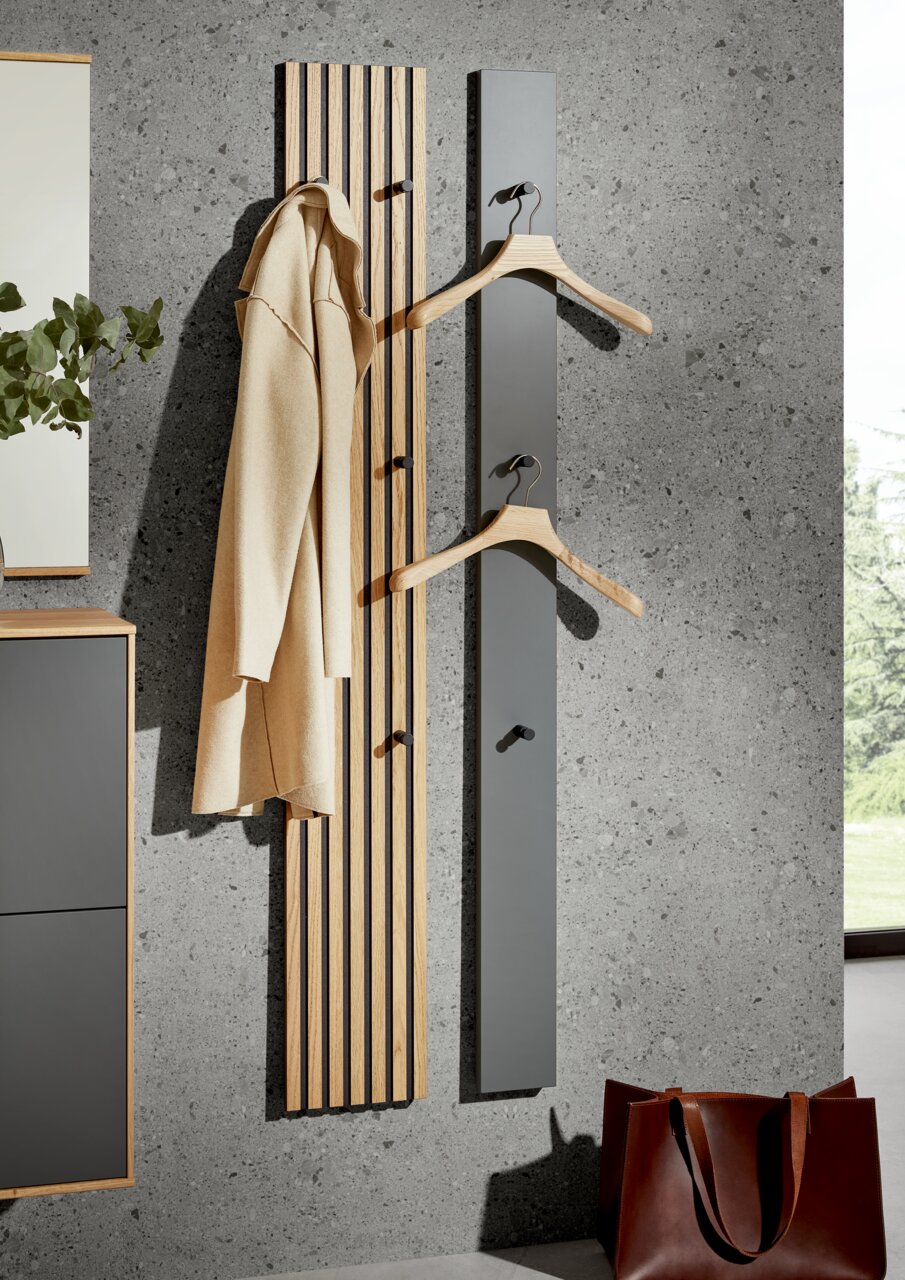 Moderne Paneel-Leiste in Holzoptik mit Haken, frontal an einer Betonwand montiert, ideal zum Aufhängen von Kleidung.