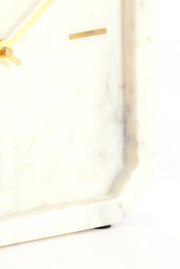 Nahaufnahme einer eleganten Uhr mit einem Zifferblatt aus weißem Marmor und goldenen Zeigern, seitliche Perspektive.
