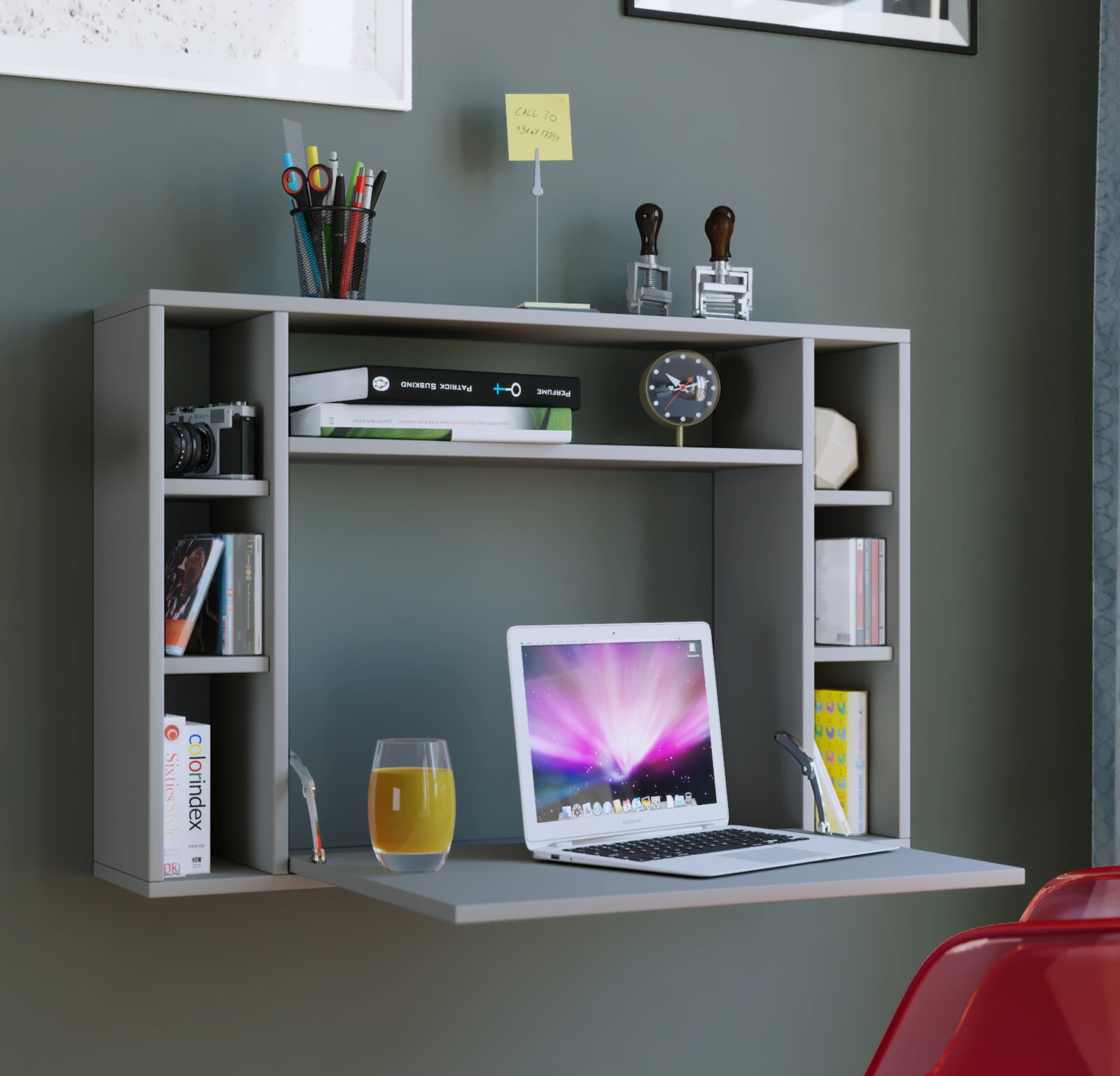 Graues Wand-Schreibtischregal mit ausklappbarer Arbeitsfläche, darauf ein Laptop und ein Glas Saft; Bücher und Deko in den Fächern, frontal aus leicht erhöhter Perspektive aufgenommen.