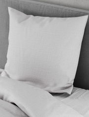 Nahaufnahme einer grauen Bettwäsche mit Kissen und Decke auf einem Bett.