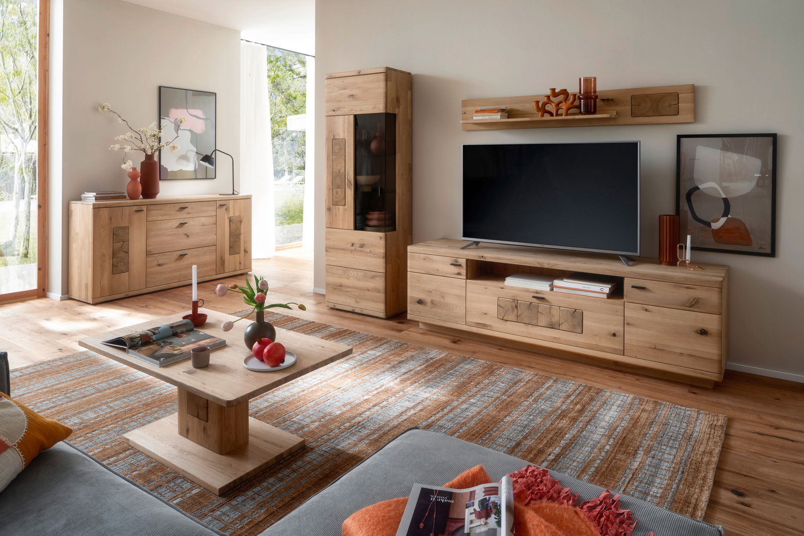 Wohnzimmer mit moderner Holzmöbelkombination, bestehend aus Sideboard, Vitrine, TV-Board und Couchtisch, in einer hellen und gemütlichen Atmosphäre. Perspektive von vorne.