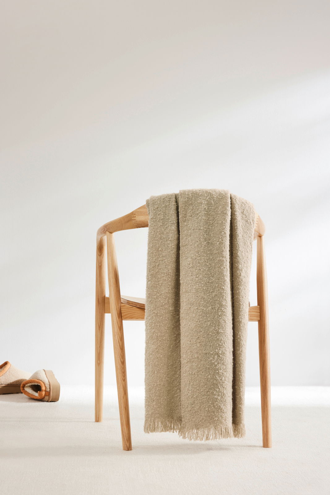 Beige Wohndecke 150x200cm auf einem Holzstuhl drapiert, seitliche Perspektive