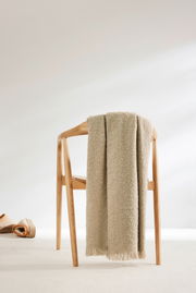 Beige Wohndecke 150x200cm auf einem Holzstuhl drapiert, seitliche Perspektive