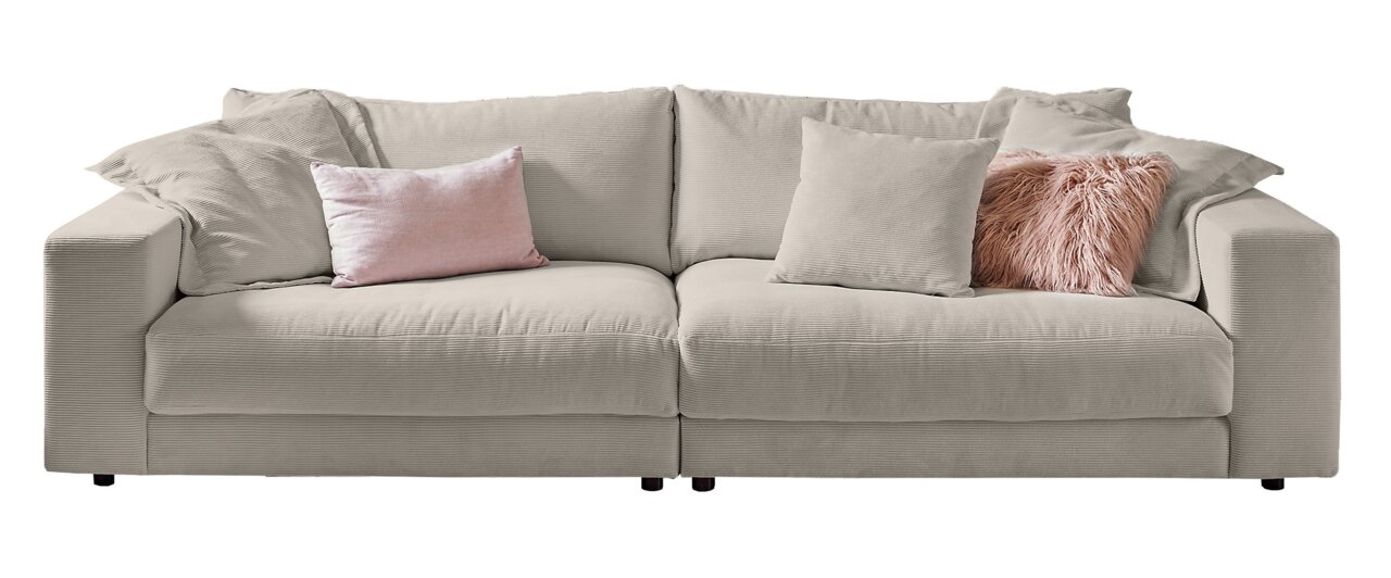 Großes, beiges Sofa mit mehreren Kissen in verschiedenen Texturen und Farben, frontal betrachtet.