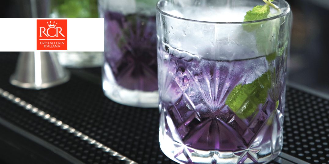 Op de bar staan twee glasheldere glazen met paarse cocktails, gegarneerd met munt.