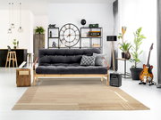 Moderner Wohnraum mit einem beigen Wollteppich im Vordergrund, der vor einem grauen Sofa liegt. Perspektive von vorne auf den Teppich.