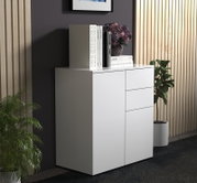 Weiße, moderne Kommode mit glatter Front und drei Schubladen in Wohnraum-Inszenierung, mit Büchern und Blumen auf der Ablage; Ansicht schräg von vorn rechts.