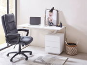 Moderner Schreibtisch mit weißer Oberfläche, seitlicher Perspektive, ausgestattet mit Laptop, Lampe und Dekorationen, neben einem ergonomischen Bürostuhl.