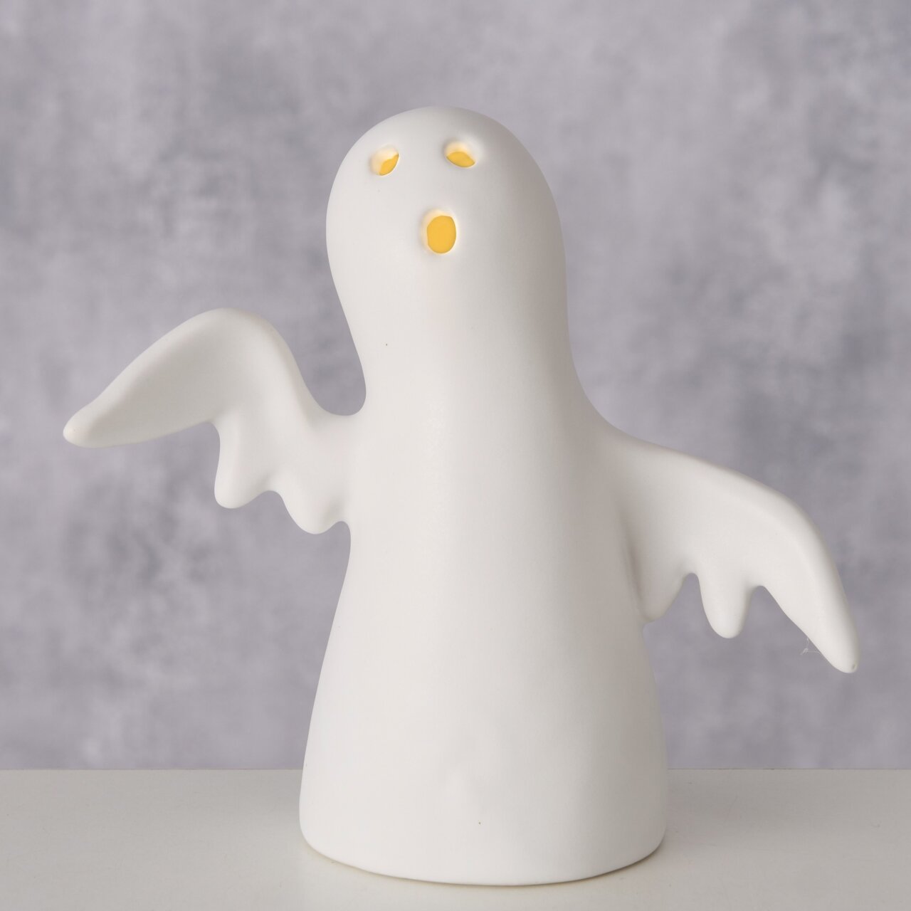Keramikfigur eines Gespensts mit ausgebreiteten Flügeln, frontal betrachtet, mit leuchtenden Augen und Mund.