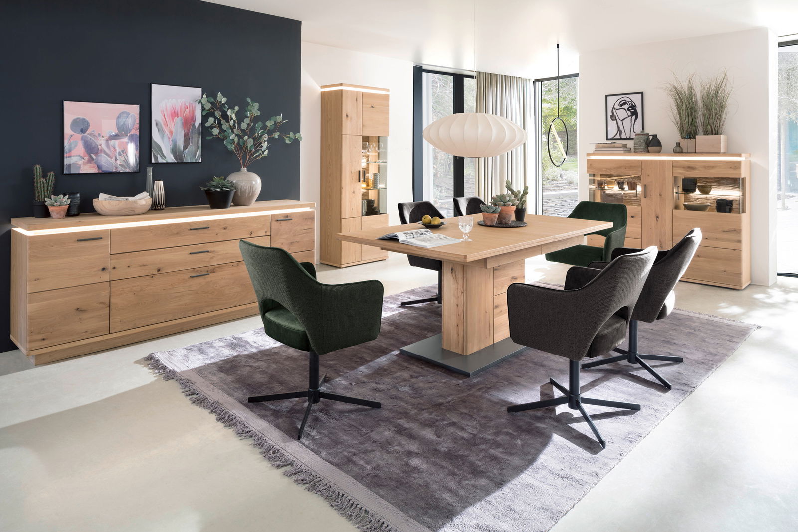 Moderne Wohnzimmereinrichtung mit Esstisch, Sideboard und Vitrine aus Holz in einem hellen Raum mit großen Fenstern, seitliche Perspektive.