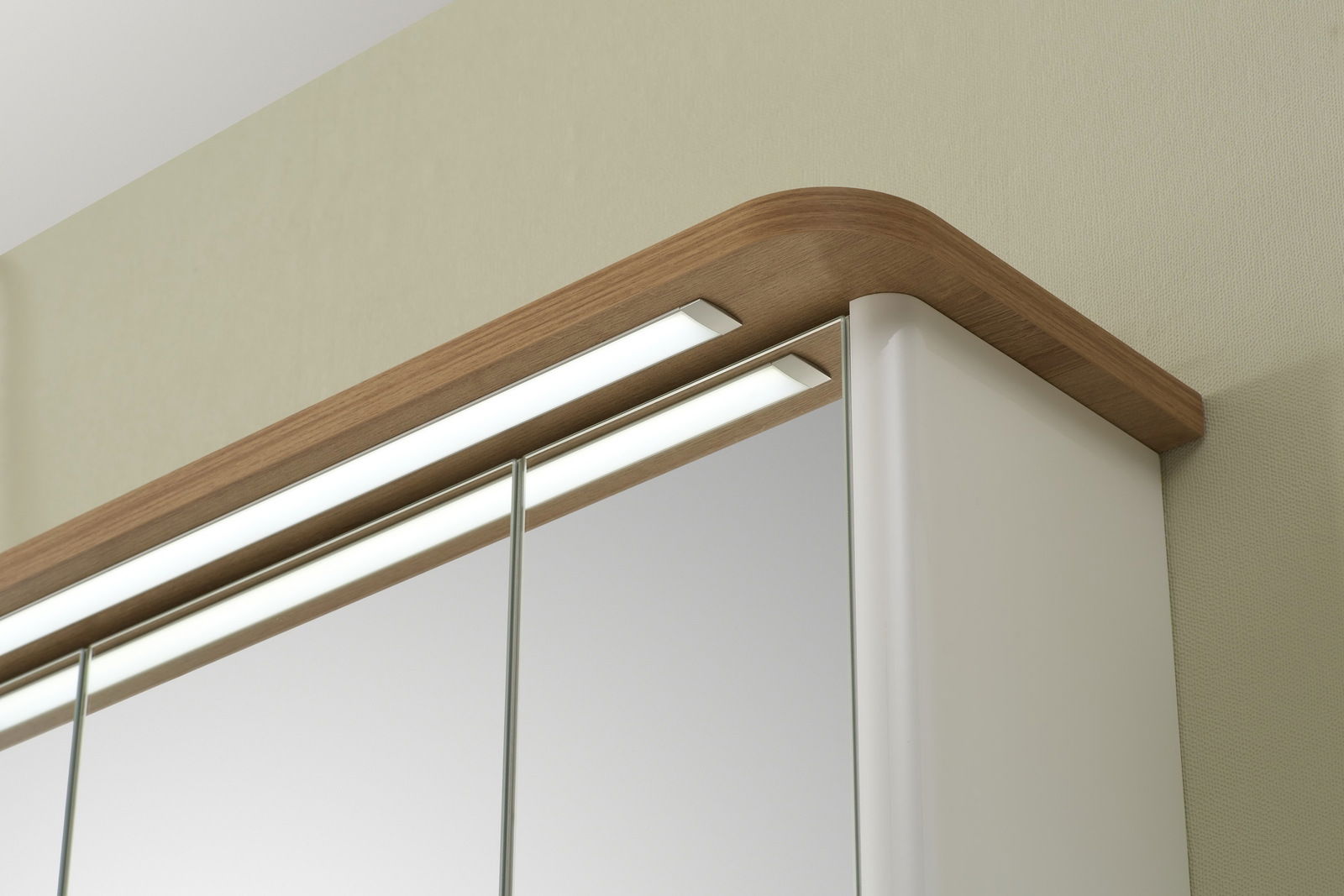 Nahaufnahme eines Spiegelschranks mit Holzrahmen und integrierter Beleuchtung von oben.